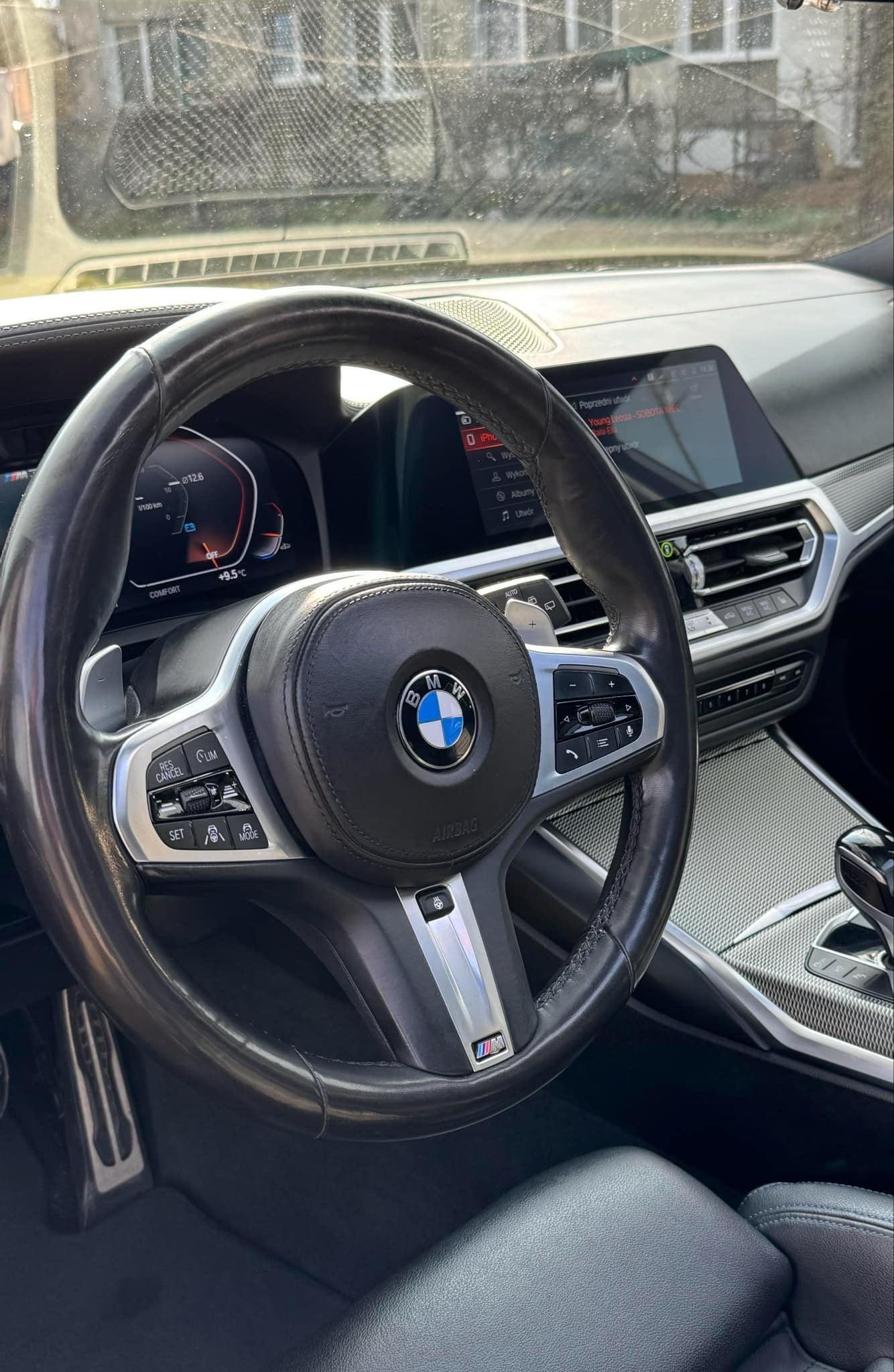 Wnętrze luksusowego BMW z czarną skórzaną tapicerką i kierownicą. Widoczne detale deski rozdzielczej i ekran dotykowy. Elementy wykończenia w kolorze srebrnym.