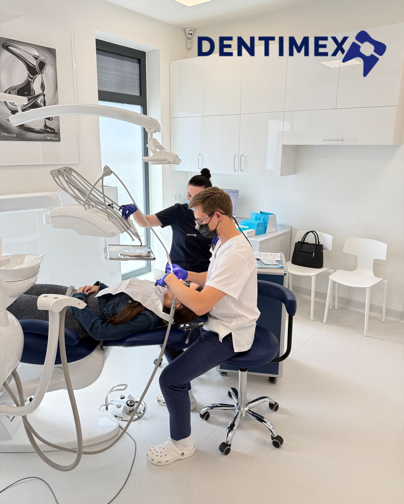 Nowoczesny gabinet stomatologiczny Dentimex: dentysta w masce i asystentka podczas zabiegu na pacjencie leżącym na niebieskim fotelu. Minimalistyczny wystrój, białe meble.