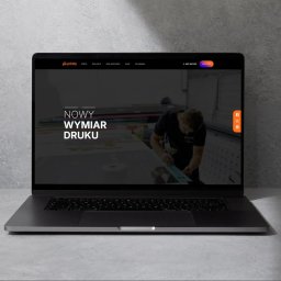 Aleksandra Godlewska Papaja Studio - Laptop prezentuje stronę internetową drukarni Printly z hasłem 'Nowy Wymiar Druku' i zdjęciem pracownika przy pracy. Widoczne logo, menu i ikony social media.