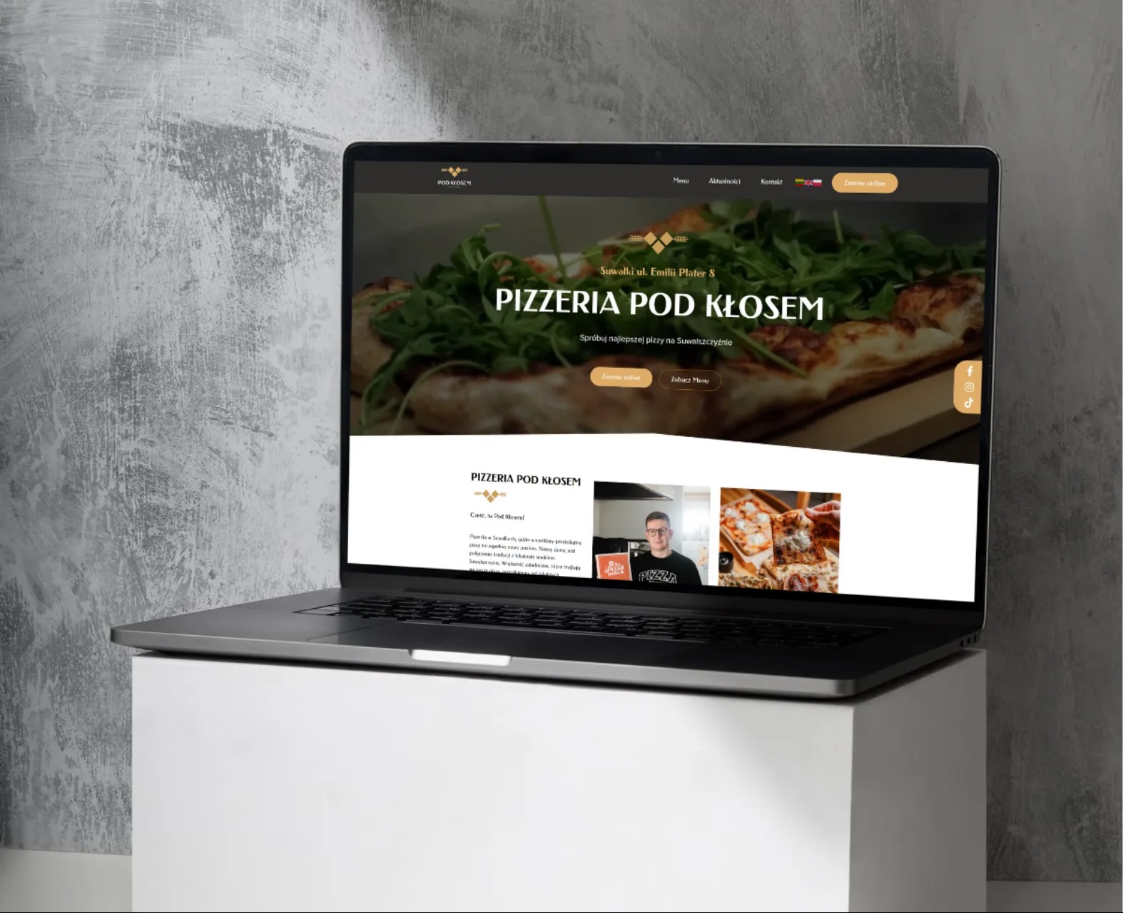 Laptop prezentuje stronę internetową pizzerii 'Pod Kłosem' z Suwałk. Widoczny nagłówek z pizzą i menu, a także sekcja 'O nas' z zdjęciem osoby i pizzy.