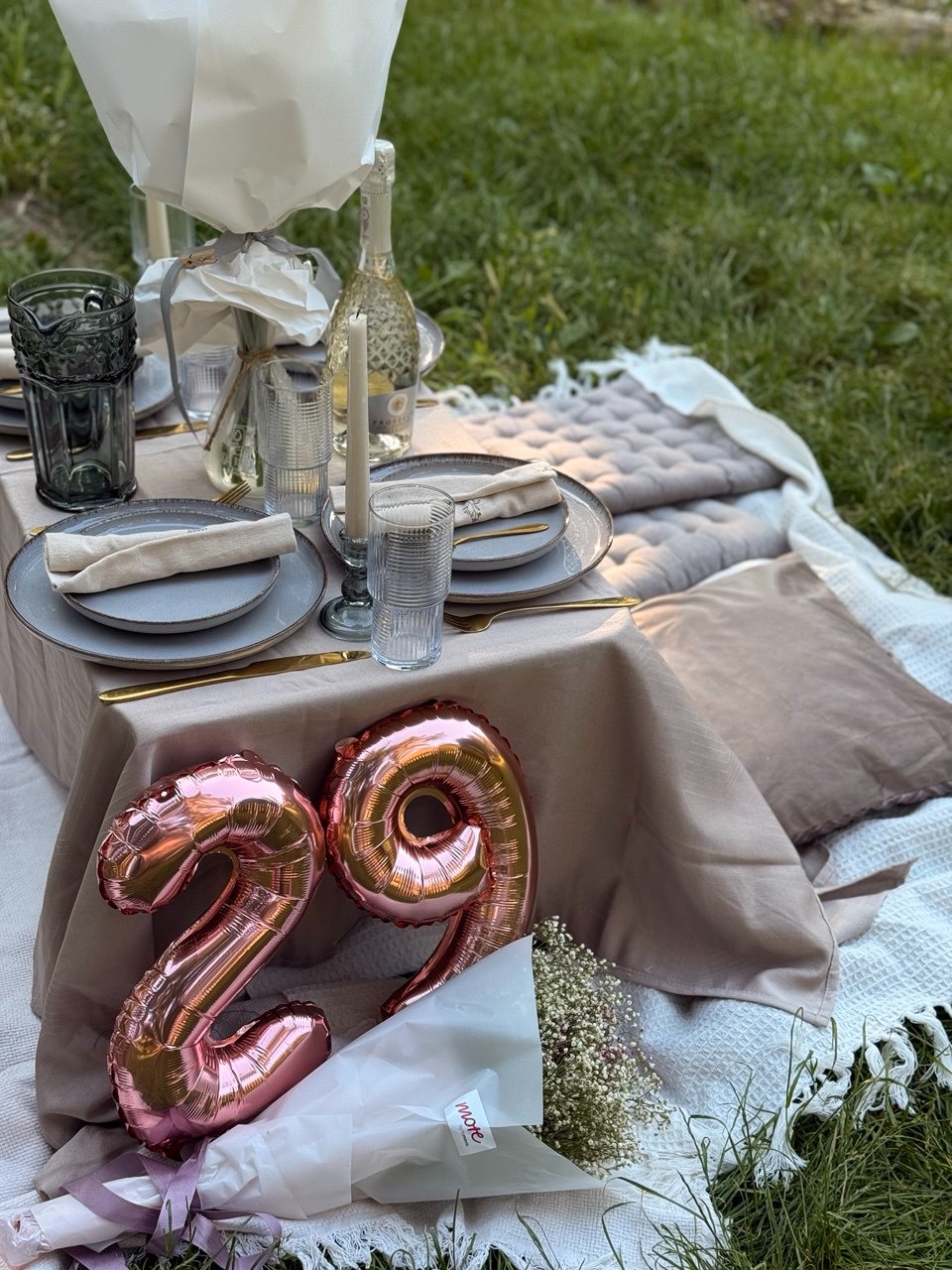Uroczysty piknik na trawie: stół z zastawą, szampan, kwiaty i balony w kształcie cyfr '29'. Romantyczna sceneria na 29 urodziny, z bliska, w plenerze.