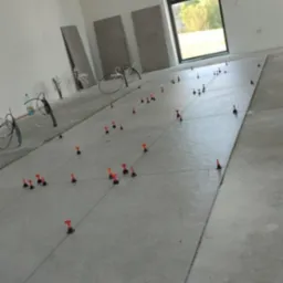 Układanie płytek podłogowych w jasnym wnętrzu z oknem. Widoczne płytki, poziomice i system poziomowania płytek. Na ścianie oparta płytka.