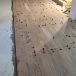 Układanie podłogi z paneli imitujących drewno z użyciem klipsów poziomujących. Widoczny fragment surowego podłoża i materiały budowlane w tle.