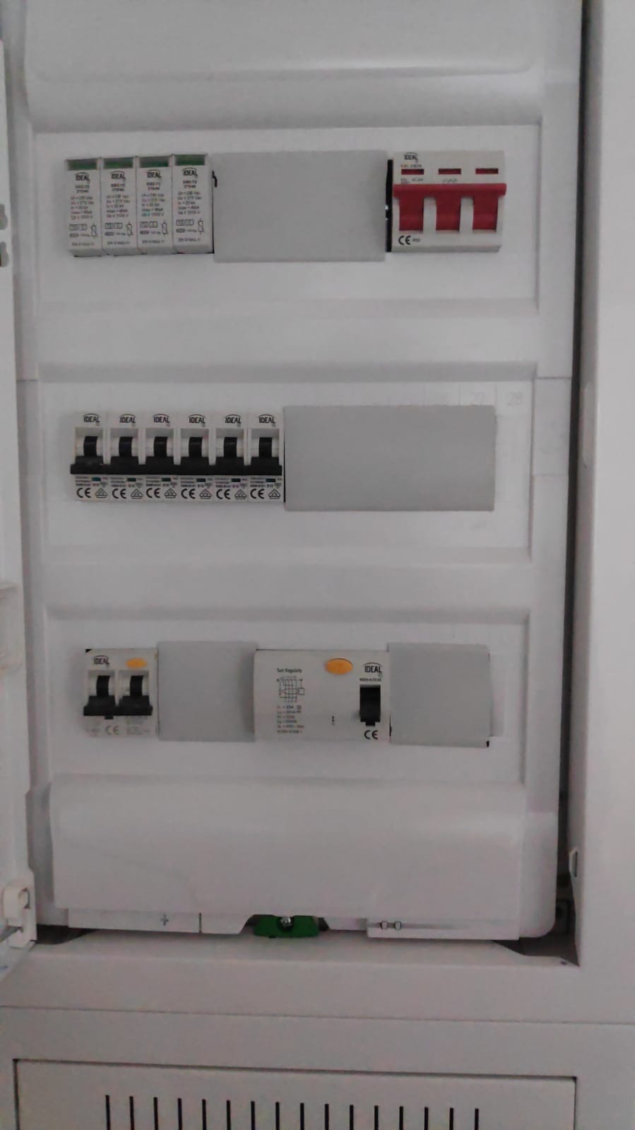 Biała skrzynka elektryczna z zainstalowanymi bezpiecznikami i wyłącznikami różnicowoprądowymi marki Ideal, widoczne oznaczenia CE. Instalacja wewnątrz budynku.