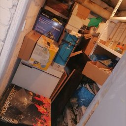 Usługi sprzątające Bombuś Marta Szczepaniak - Zagracone pomieszczenie ze stertą pudeł, sprzętów i śmieci pod ścianą. Widoczne regały z dokumentami. Perspektywa z góry.