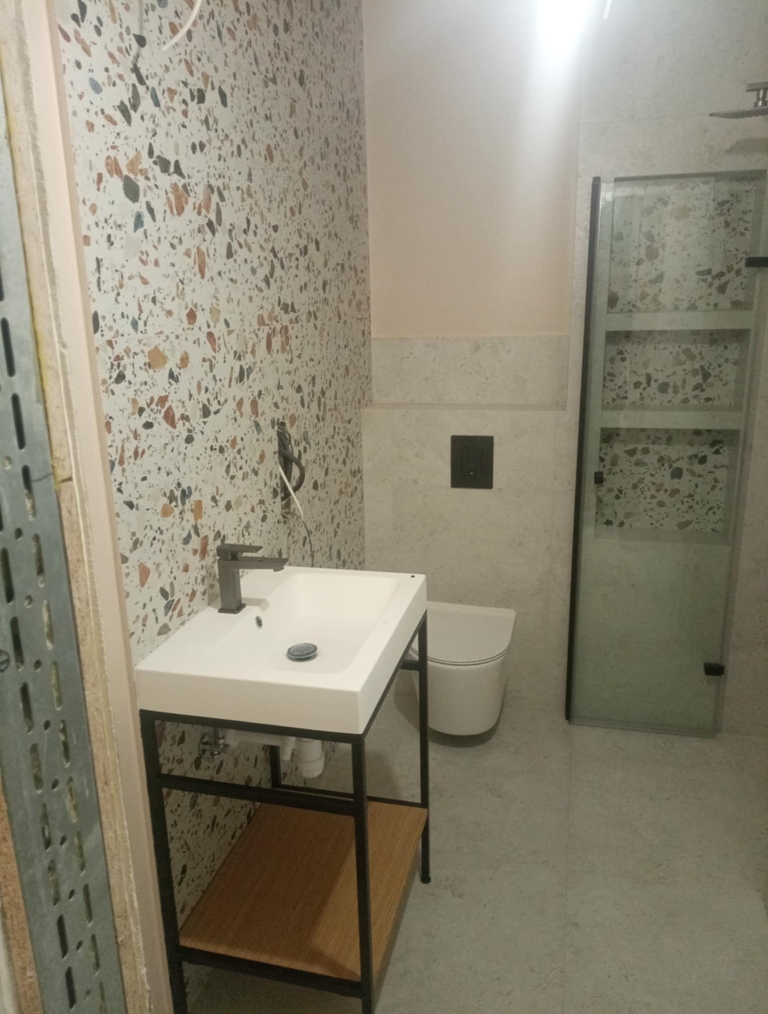 Nowoczesna łazienka z umywalką na metalowym stelażu, toaletą w zabudowie i kabiną prysznicową. Ściany wyłożone płytkami imitującymi lastryko.