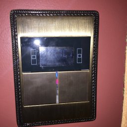 Braim Company Sp z o.o - Panel sterowania inteligentnego domu z ekranem dotykowym i ozdobną ramką, zamontowany na bordowej ścianie. Widoczne elementy interfejsu i subtelne oświetlenie.