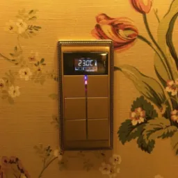 Elegancki panel sterowania inteligentnego domu z wyświetlaczem temperatury, osadzony w ścianie z kwiecistą tapetą w stylu vintage.