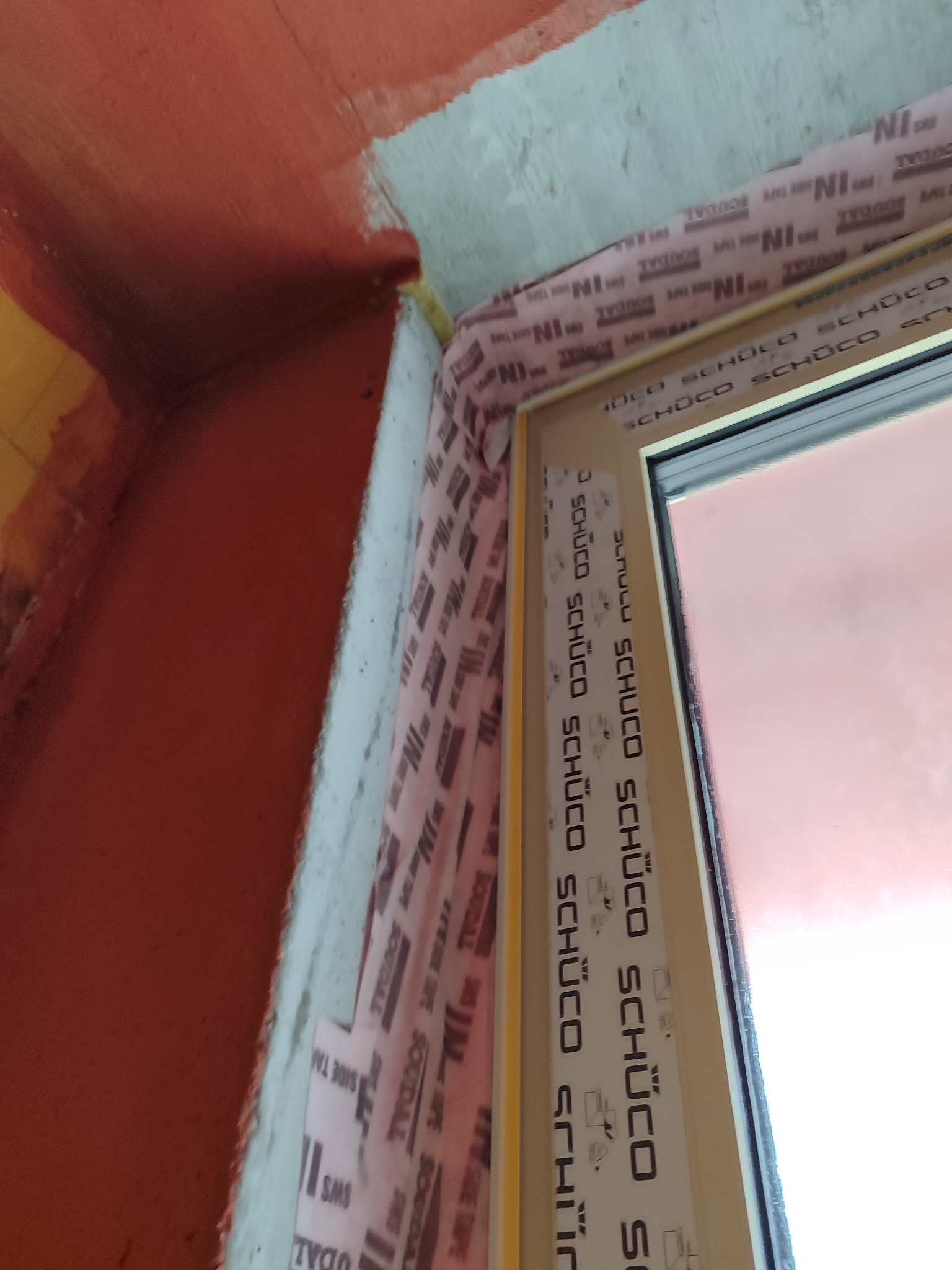 Szczegółowe ujęcie okna Schüco z uszczelnieniami Soudal, pomarańczowe tło. Kątowe ujęcie podkreśla precyzję montażu i dbałość o detale wykończenia.