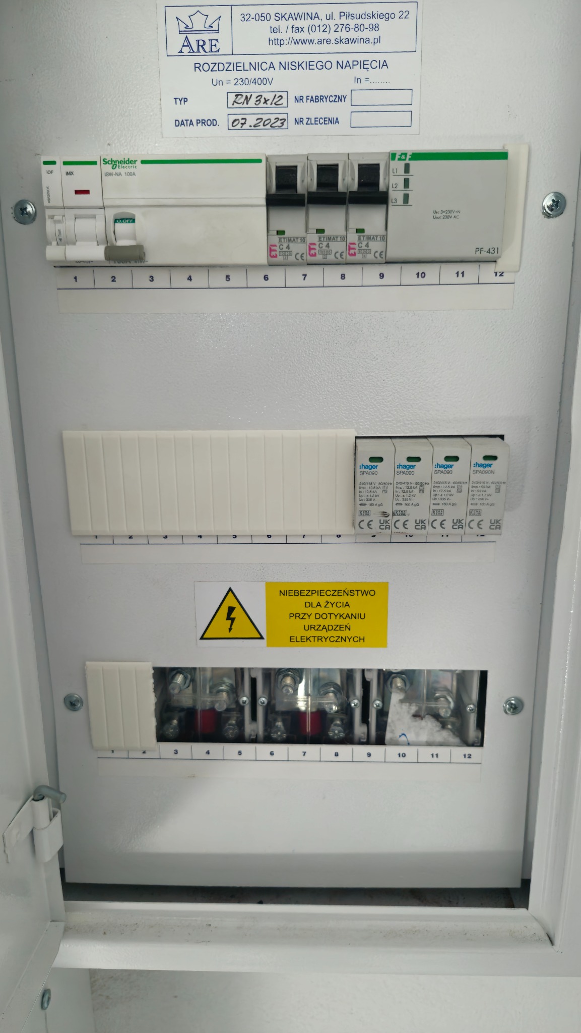 Rozdzielnica niskiego napięcia z zabezpieczeniami Hager i Schneider Electric, widoczne bezpieczniki, ograniczniki przepięć i tabliczka ostrzegawcza.