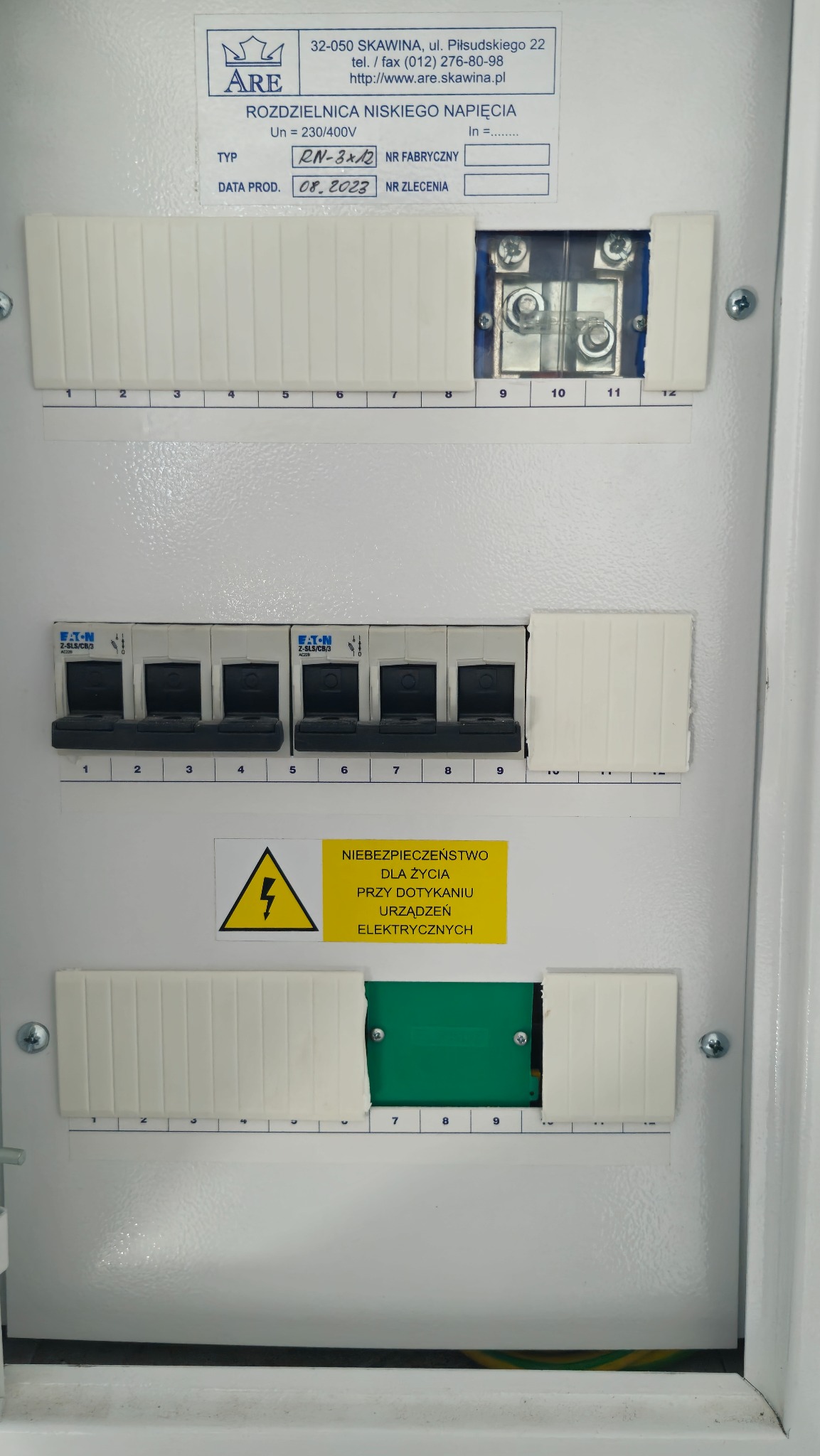 Rozdzielnica niskiego napięcia z wyłącznikami Eaton, tabliczką znamionową i ostrzeżeniem o niebezpieczeństwie porażenia elektrycznego. Widoczne elementy instalacji.