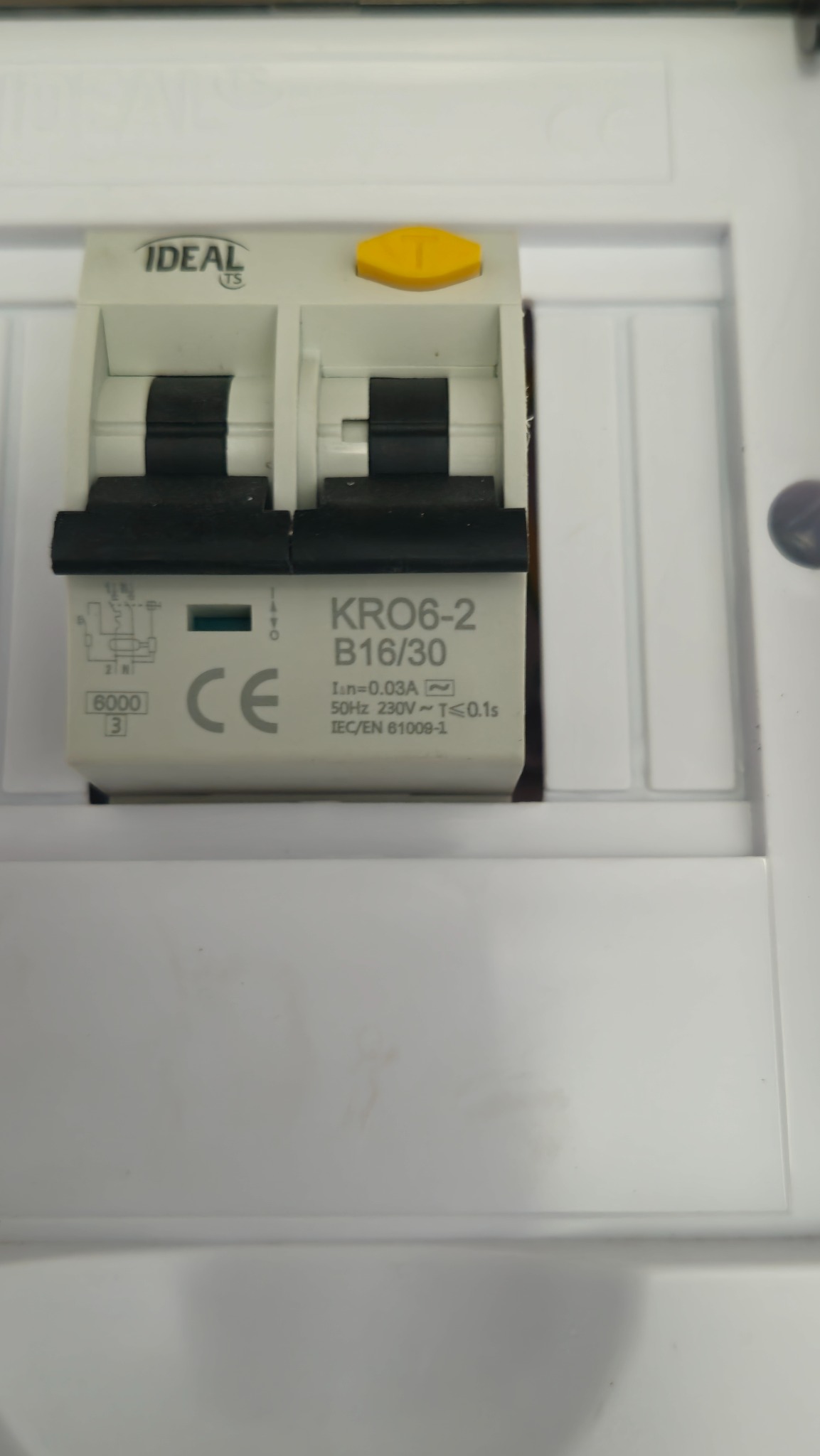 Wyłącznik różnicowoprądowy IDEAL KRO6-2 B16/30 w białej obudowie. Widoczne oznaczenia techniczne i żółty przełącznik. Ujęcie z bliska, ostre.