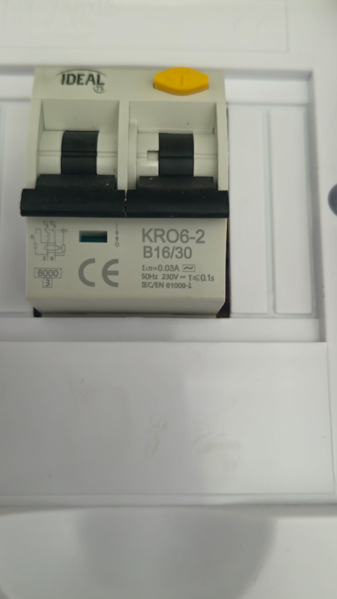 Biały wyłącznik różnicowoprądowy IDEAL TS KRO6-2 B16/30 w skrzynce, widoczne parametry techniczne i oznaczenia CE, z żółtym przyciskiem testowym.