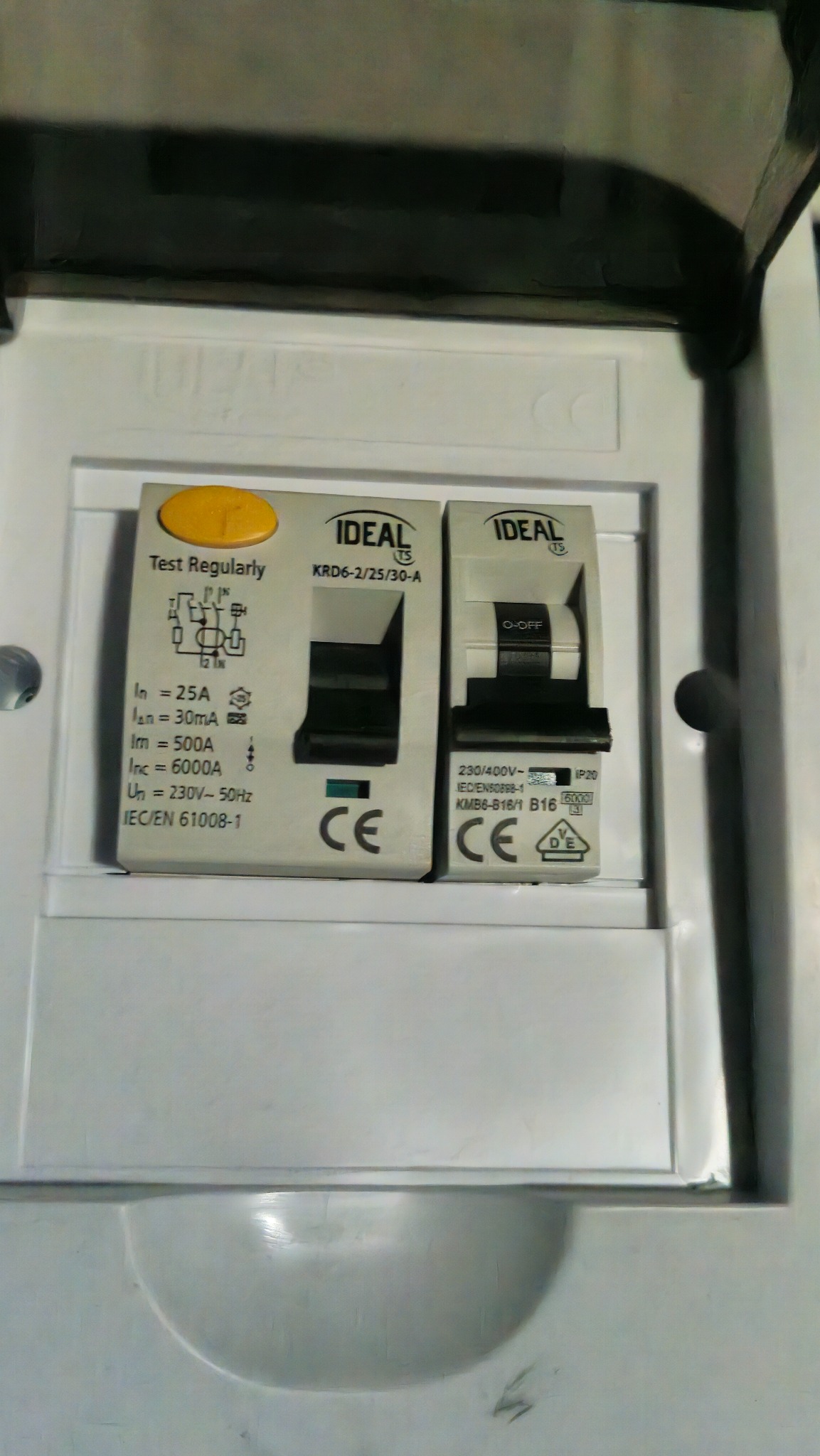 Dwa wyłączniki różnicowoprądowe marki Ideal w białej skrzynce rozdzielczej. Jeden z żółtym przyciskiem testowym, drugi z przełącznikiem w pozycji 'O-OFF'.