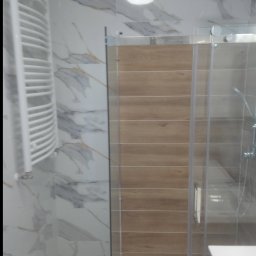 Robert Bińko usługi remontowo wykonczeniowe - Wykończona łazienka z kabiną prysznicową z drewnianym panelem, grzejnikiem drabinkowym i marmurowymi płytkami. Nowoczesny design, jasne oświetlenie.