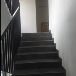 Ciemne, marmurowe schody z czarną, metalową balustradą w nowoczesnym wnętrzu. Na ścianie widoczny obrazek autobusu, oświetlony górnym światłem.