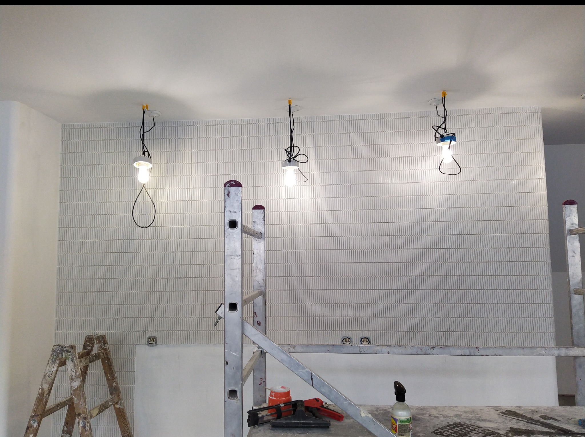 Układanie płytek w pionowy wzór w mieszkaniu we Wrocławiu. Widoczne rusztowanie i narzędzia, tymczasowe oświetlenie. Praca glazurnicza w toku.