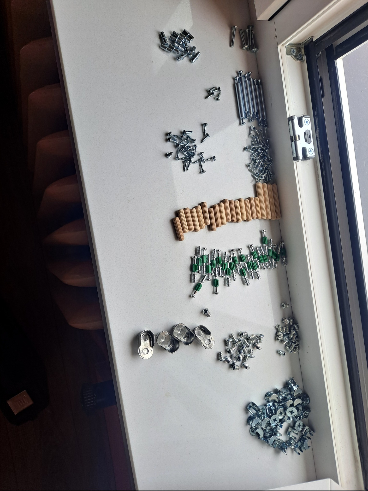 Akcesoria do montażu mebli, widoczne śruby, kołki i inne elementy na białym blacie w Bytomiu. Przygotowanie do skręcania.