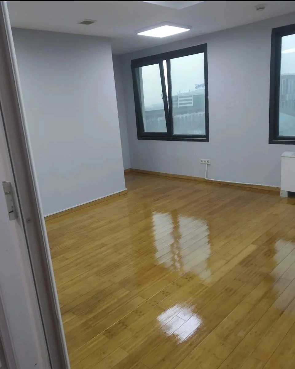 Jasny pokój po odświeżeniu: świeżo pomalowane szare ściany, parkiet odbijający światło, duże okna z widokiem na miasto w tle.