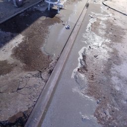 SPAW-BUD - Mokry beton na podłodze, z widocznymi elementami konstrukcyjnymi i fragmentami gruzu. Ślady naprawy lub wylewki betonu na nierównej powierzchni.