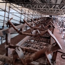 SPAW-BUD - Wnętrze w trakcie prac remontowych: widok na rusztowania z metalową siatką podłogową, konstrukcja wsporcza i ściana w tle. Ujęcie z dołu w górę.