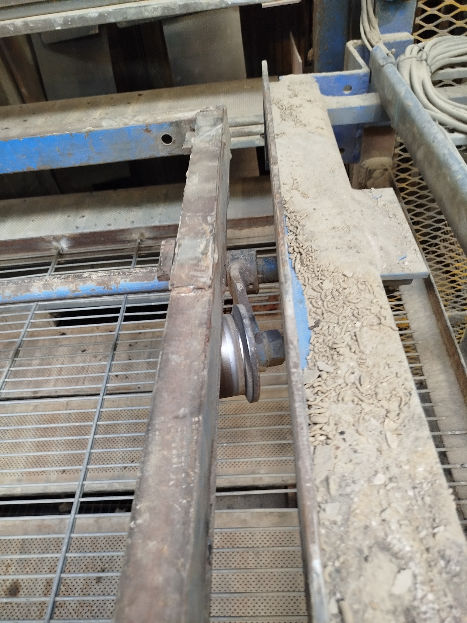 Metalowa konstrukcja z kołem, pokryta kurzem i zabrudzeniami, z elementami niebieskiej farby. Widoczna kratownica w tle.