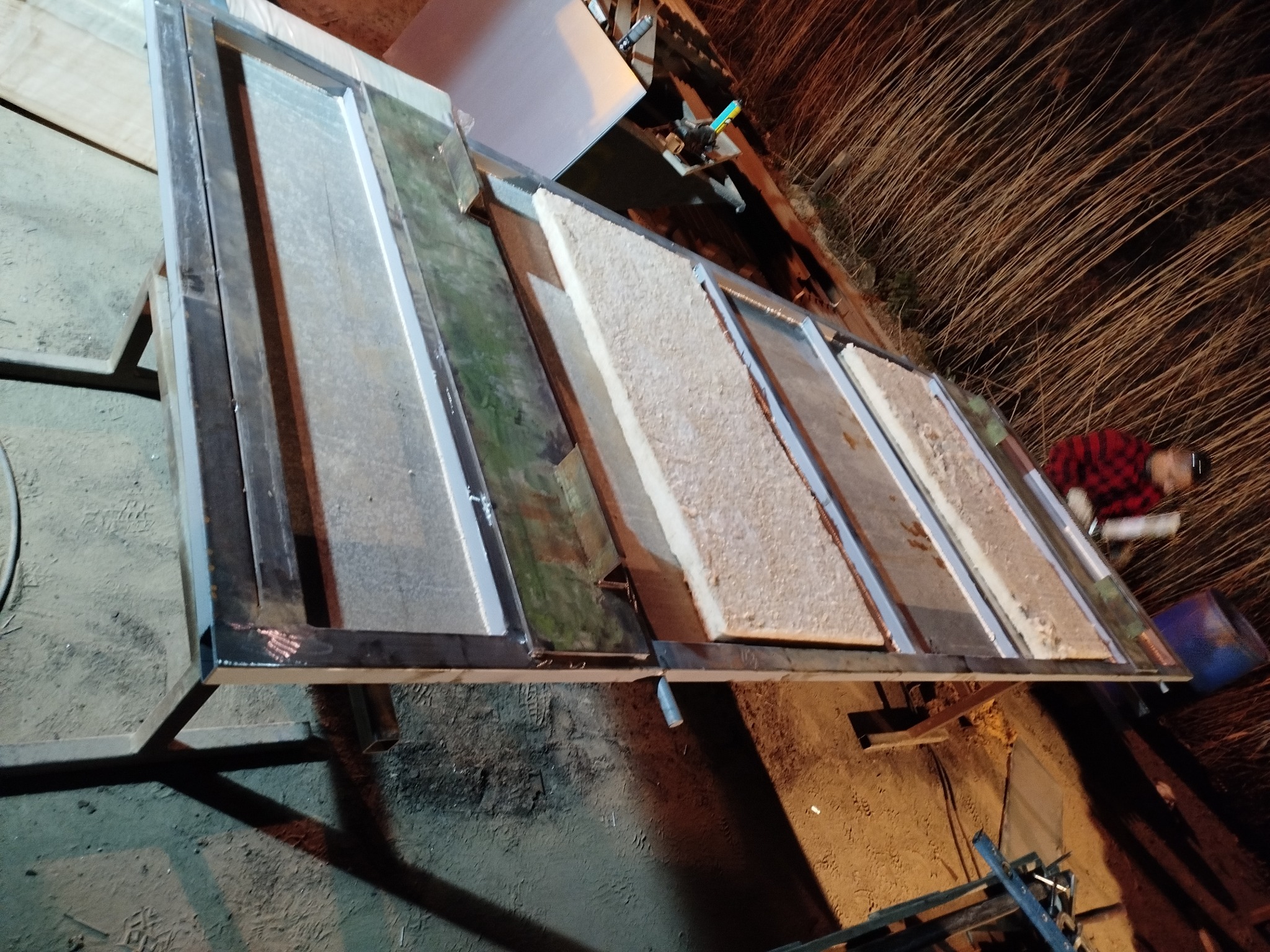 Konstrukcja metalowa z wypełnieniami z płyt, prawdopodobnie w trakcie tworzenia ścianki działowej lub elementu wykończenia wnętrz. Widoczny pracownik w tle.