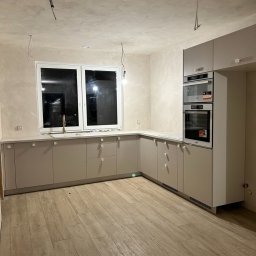 VertoAir - Jasna kuchnia z drewnianą podłogą i nowoczesną zabudową. Widoczne niedokończone prace elektryczne na suficie i ścianach. Minimalistyczny design.