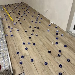 VertoAir - Układanie paneli podłogowych z ogrzewaniem podłogowym, z użyciem systemu poziomowania płytek. Widoczna poziomica i fragment instalacji grzewczej.