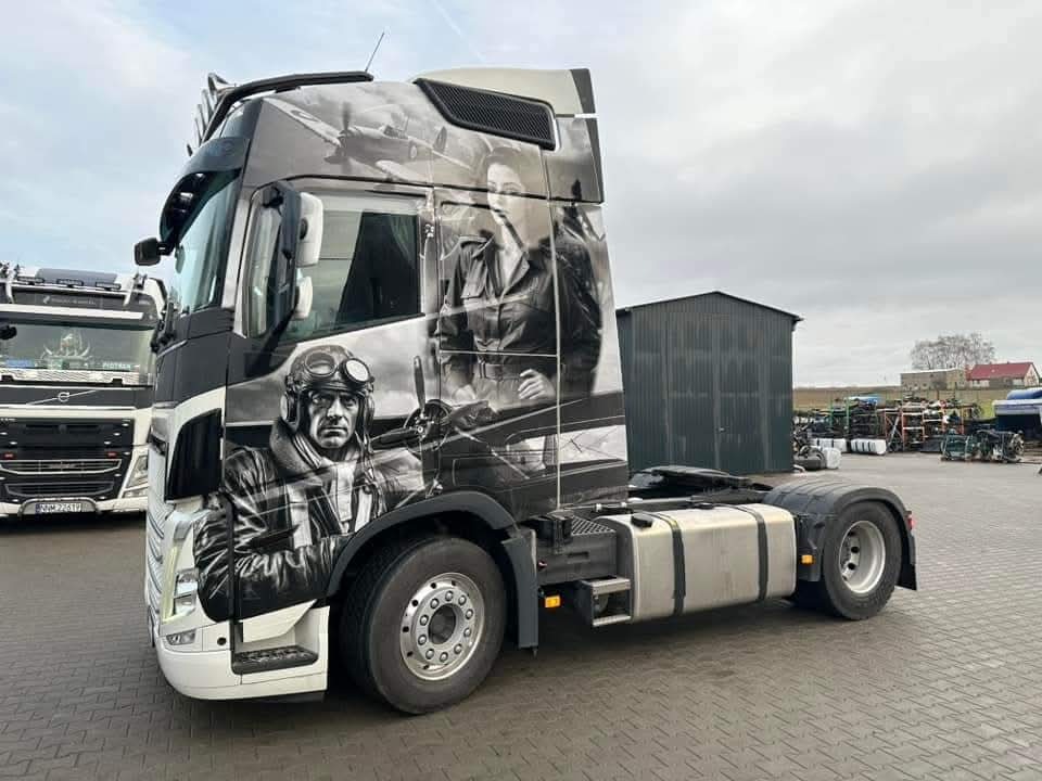 Ciężarówka z grafiką lotniczą w stylu retro: pilot w goglach i kobieta w skórzanej kurtce na tle samolotów. Czarno-biała kompozycja na kabinie.