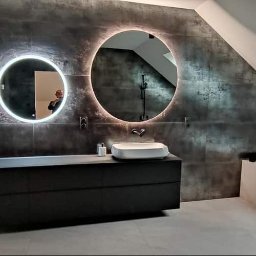 Perfect Home Remonty i wykończenia wnętrz - Nowoczesna łazienka na poddaszu z okrągłymi lustrami z podświetleniem LED, ciemnymi płytkami imitującymi metal i minimalistyczną białą armaturą. Częściowo wykończone wnętrze.