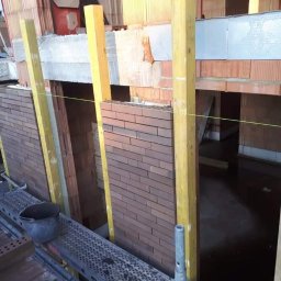 Perfect Home Remonty i wykończenia wnętrz - Murowanie ściany z cegły klinkierowej na budowie. Widoczne rusztowanie, podpory i sznurek murarski. W tle ściany z pustaków ceramicznych.