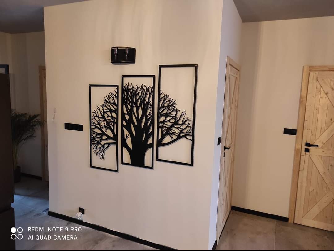 Nowoczesne wykończenie wnętrza: dekoracja ścienna z motywem drzewa w czarnych ramach, drewniane drzwi w stylu rustykalnym i minimalistyczne oświetlenie.