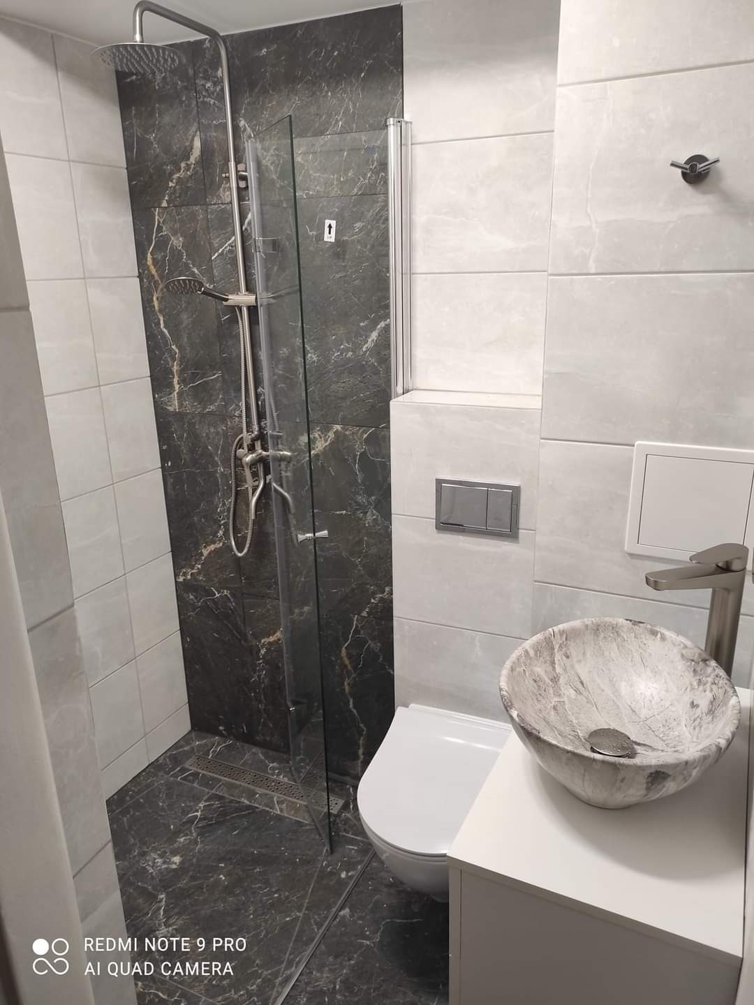 Wykończona łazienka z kabiną typu walk-in i marmurową okładziną. Umywalka w kształcie misy na blacie. Nowoczesna armatura w kolorze szczotkowanego metalu.