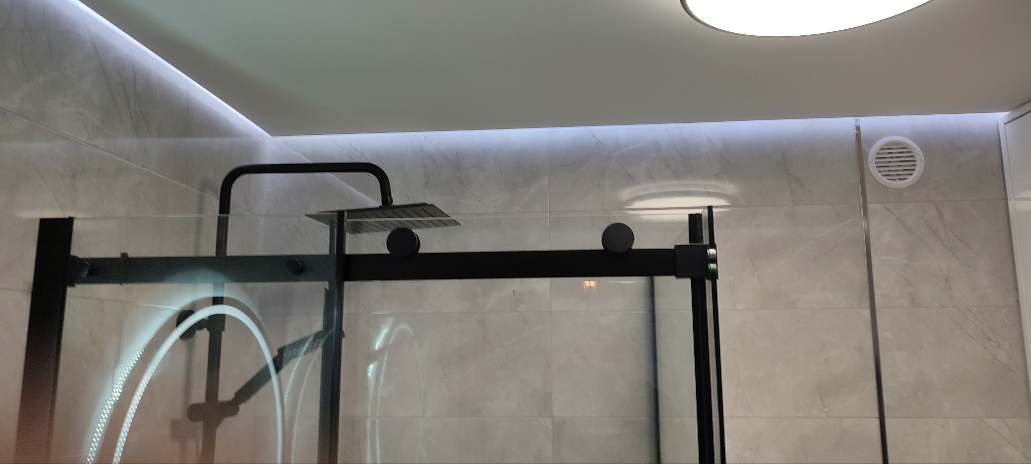 Nowoczesna kabina prysznicowa z czarnymi profilami i deszczownicą, oświetlenie LED wzdłuż sufitu, marmurowe płytki ścienne. Wykończenie łazienki.