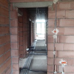 LANGOLD SPÓŁKA Z OGRANICZONĄ ODPOWIEDZIALNOŚCIĄ - Wnętrze w trakcie prac: korytarz z widoczną instalacją elektryczną w peszlach na podłodze i puszkami w ścianach z czerwonej cegły. Stan surowy.