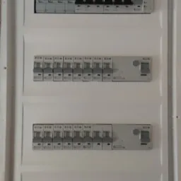 Rozdzielnica elektryczna z zainstalowanymi bezpiecznikami Eaton i Hager, widoczne oznaczenia numerów obwodów. Gotowa instalacja w białej obudowie.