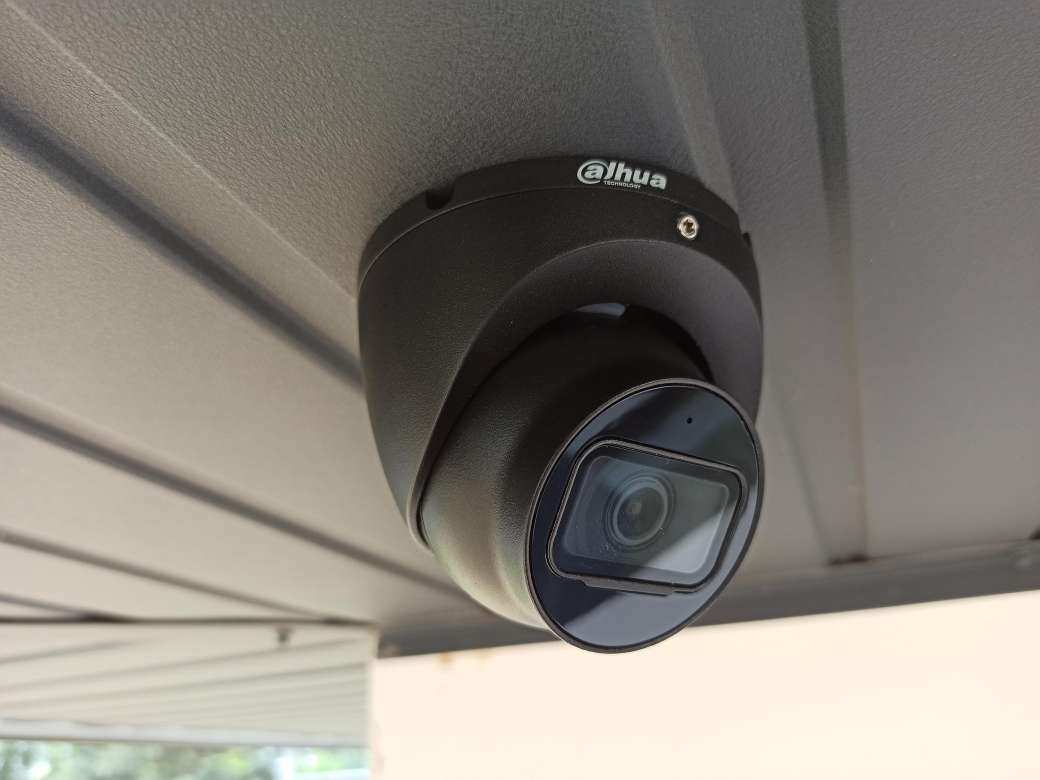 Zamontowana kamera kopułkowa Dahua, czarna, przymocowana do szarego sufitu z blachy trapezowej. Widok z dołu, obiektyw skierowany w dół.