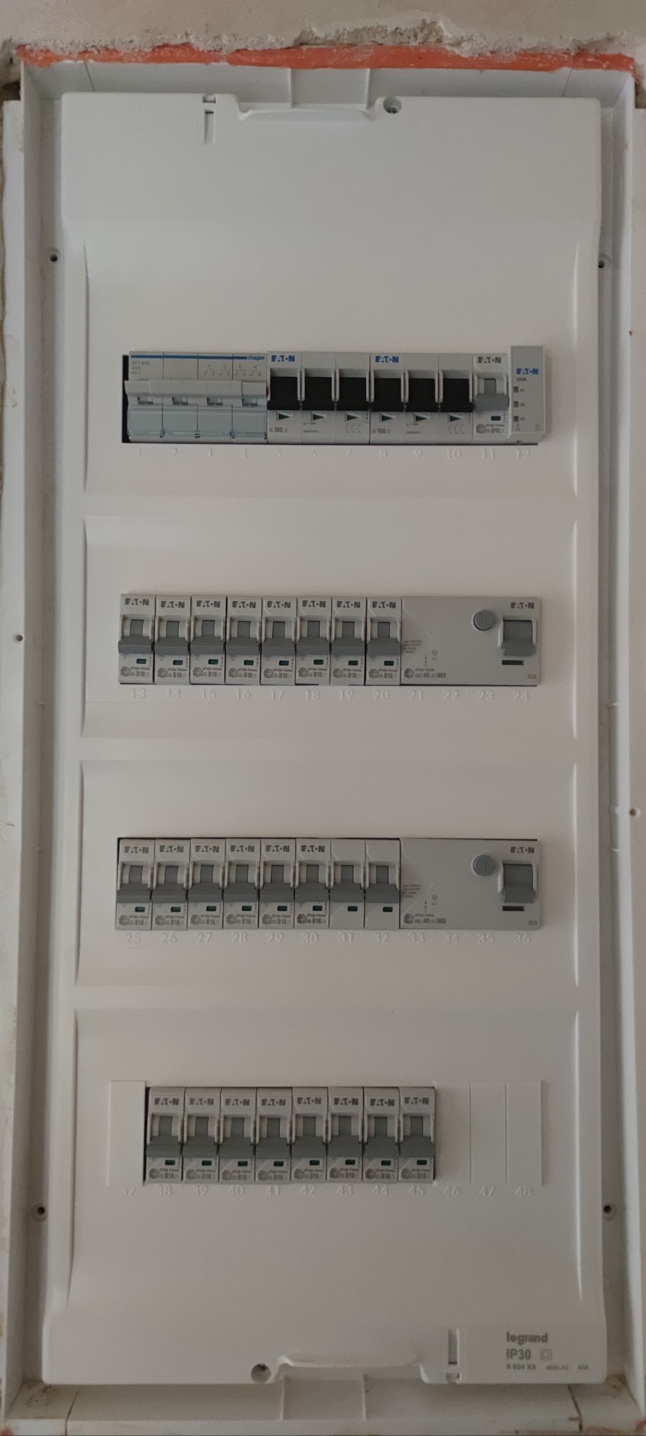 Rozdzielnica elektryczna z zainstalowanymi bezpiecznikami Eaton i Hager, widoczne oznaczenia numerów obwodów. Gotowa instalacja w białej obudowie.