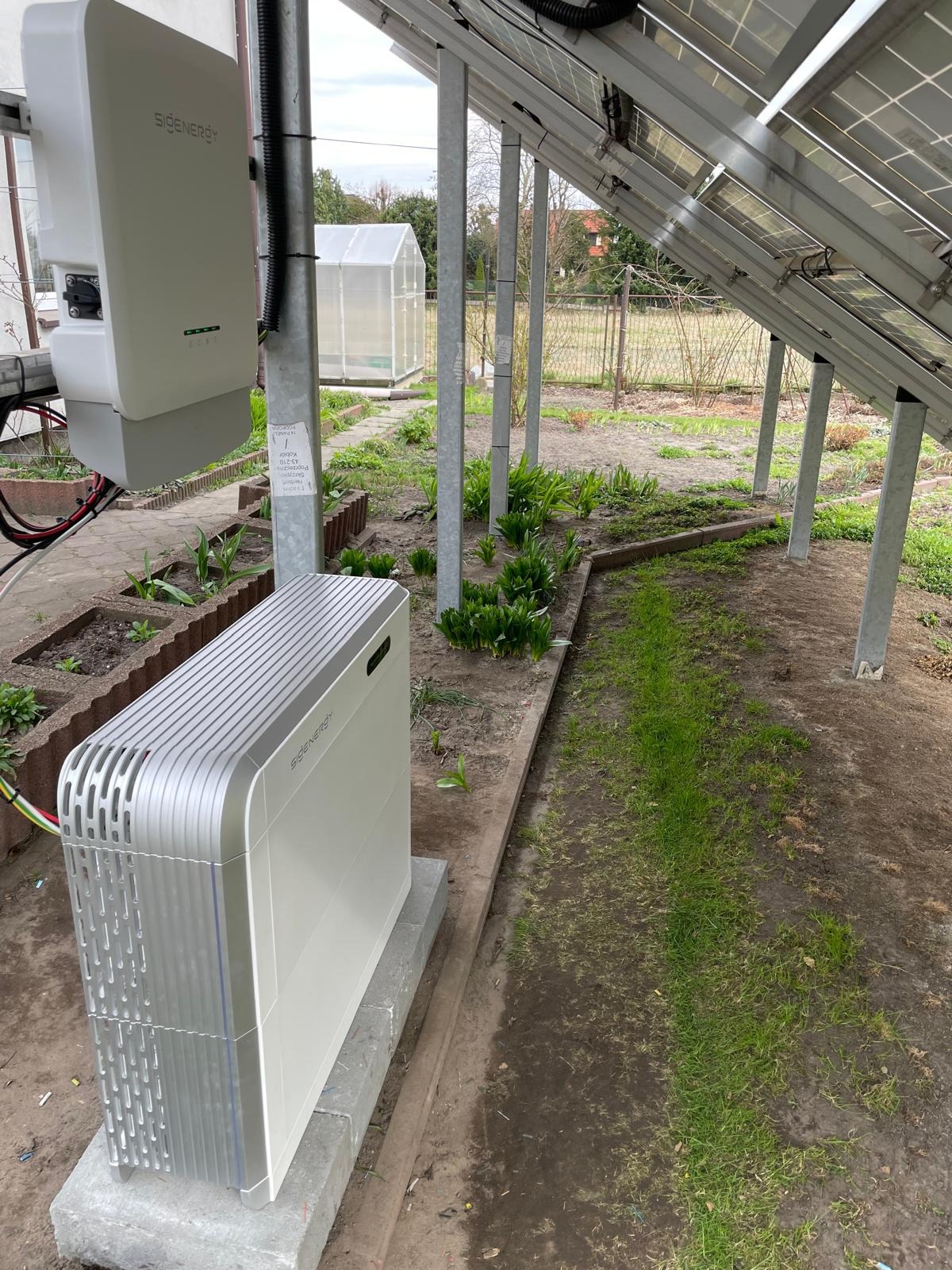 Instalacja magazynu energii Sigenenergy obok paneli słonecznych w ogrodzie. Widoczny inwerter i moduł bateryjny na betonowym fundamencie.