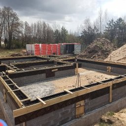 Mykhailo Olenich - Częściowo wylane fundamenty budynku z widocznym zbrojeniem, szalunkiem, izolacją i bloczkami betonowymi. Na drugim planie hałdy piachu i materiały budowlane.