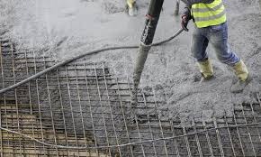 Wylewanie betonu na siatkę zbrojeniową, widoczne buty robocze i fragment węża do betonu. Prace w toku, szara kolorystyka, duży format siatki.