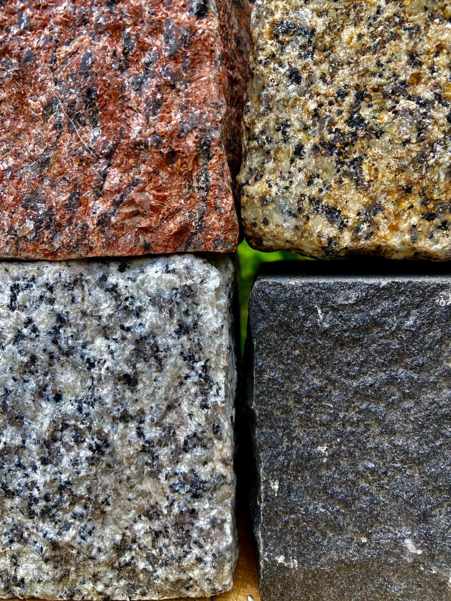 Zbliżenie na cztery kostki brukowe o różnej kolorystyce i fakturze, ułożone obok siebie. Widoczne detale kamienia: czerwony, beżowy, szary i grafitowy.