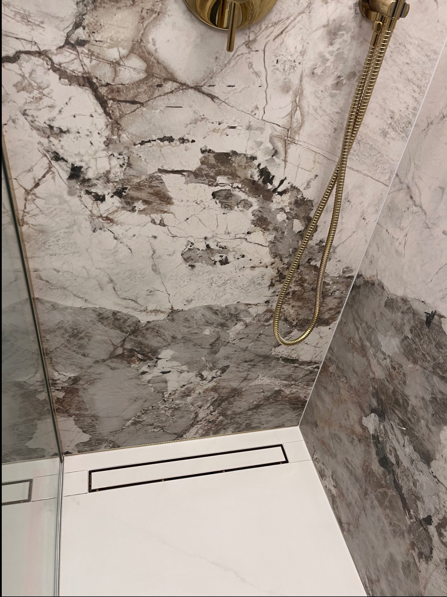 Wykończona łazienka z marmurowymi płytkami, złotą armaturą i odpływem liniowym. Nowoczesny design z dbałością o detale.