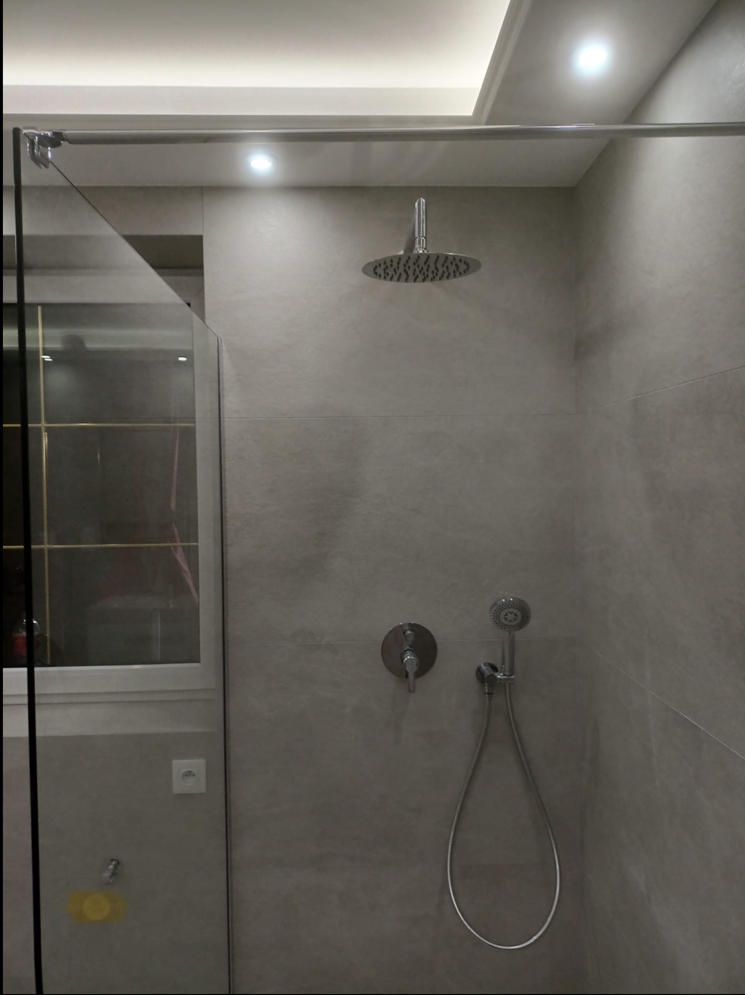 Nowoczesna kabina prysznicowa z deszczownicą i szklaną ścianką, wykończona szarymi płytkami. Minimalistyczny design, oświetlenie punktowe w suficie.