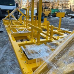 FERROTECH SPÓŁKA CYWILNA - Żółta, metalowa konstrukcja nośna, owinięta folią ochronną, na zewnątrz. W tle widoczny wózek widłowy i samochód dostawczy. Konstrukcja spawana i pomalowana.