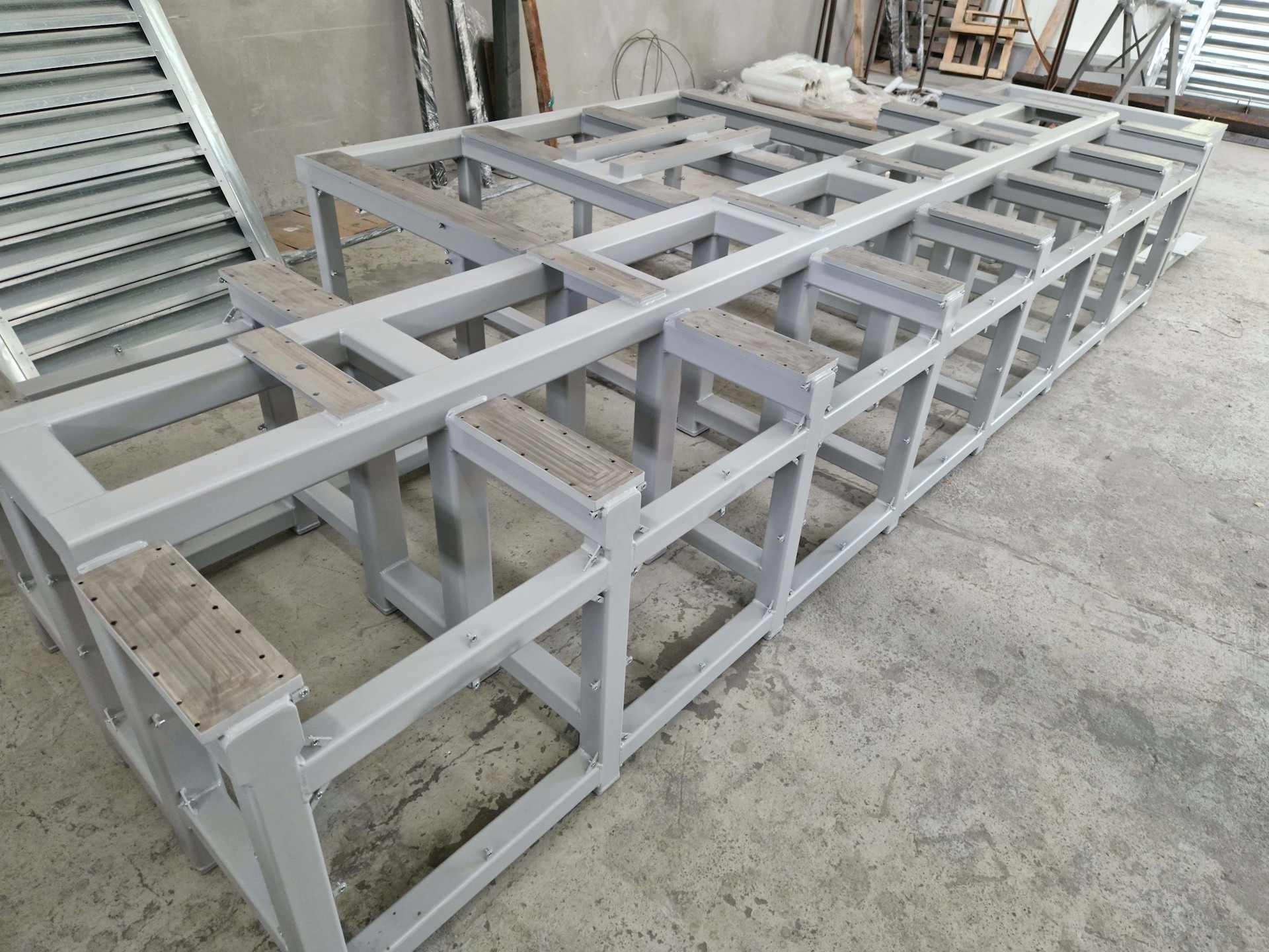 Szara, metalowa konstrukcja szkieletowa z drewnianymi elementami, spawana, widok z perspektywy, na betonowej posadzce w hali.