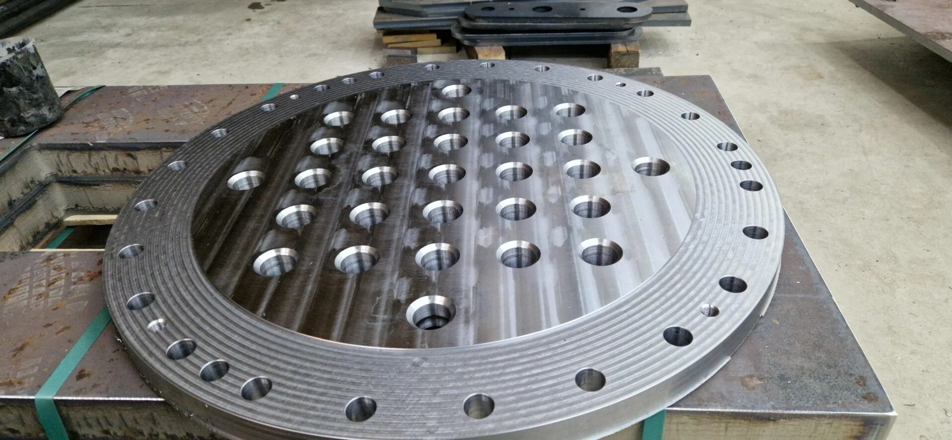 Obróbka CNC: Okrągły, metalowy element z precyzyjnie wywierconymi otworami, leżący na metalowym stole. Widoczne ślady obróbki skrawaniem.