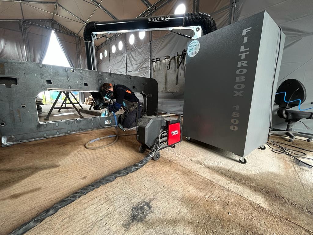 Spawanie konstrukcji stalowej w hali namiotowej. Widoczny spawacz w masce, urządzenie spawalnicze Lincoln i filtr powietrza Filtrobox 1500.