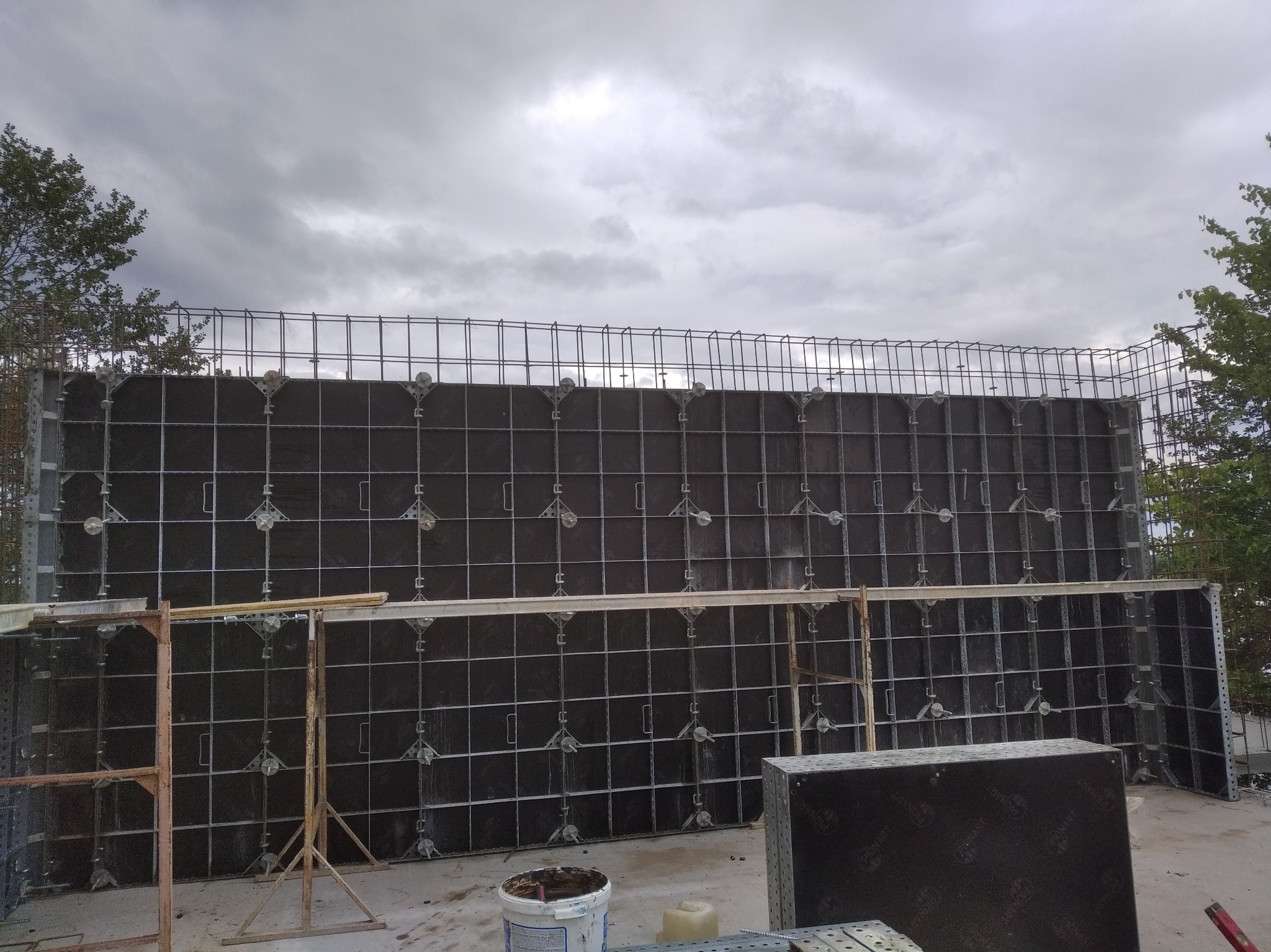 Szare szalunki zbrojeniowe na budowie domu, widoczne elementy konstrukcyjne i niebo z chmurami. Etap przygotowania do wylewania fundamentów.